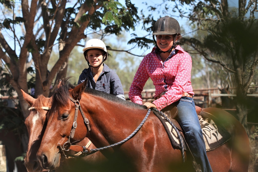 Two happy kids - one boy, one girl - sit on horses next to each other in full riding gear.
