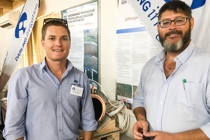 Graham Robinson and Trevor Brown in front of signs at Trangie ag station workshop