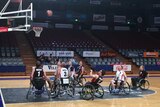 Wheelchair basketball players watch as a ball approaches the net