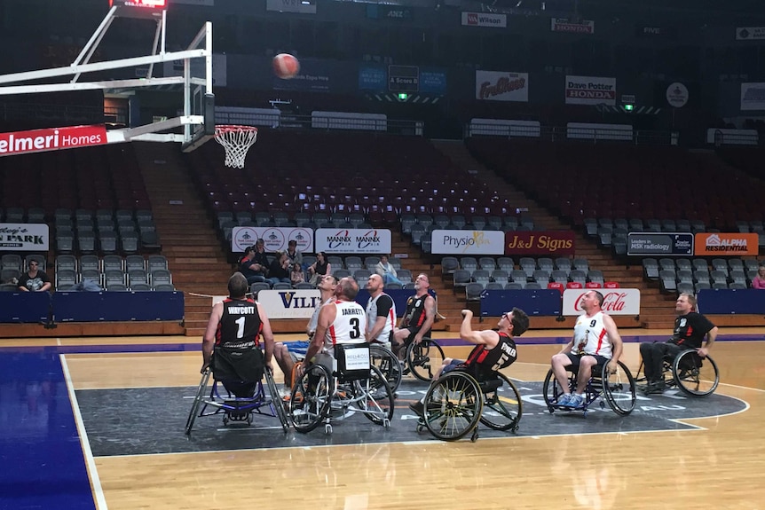 Wheelchair basketball players watch as a ball approaches the net