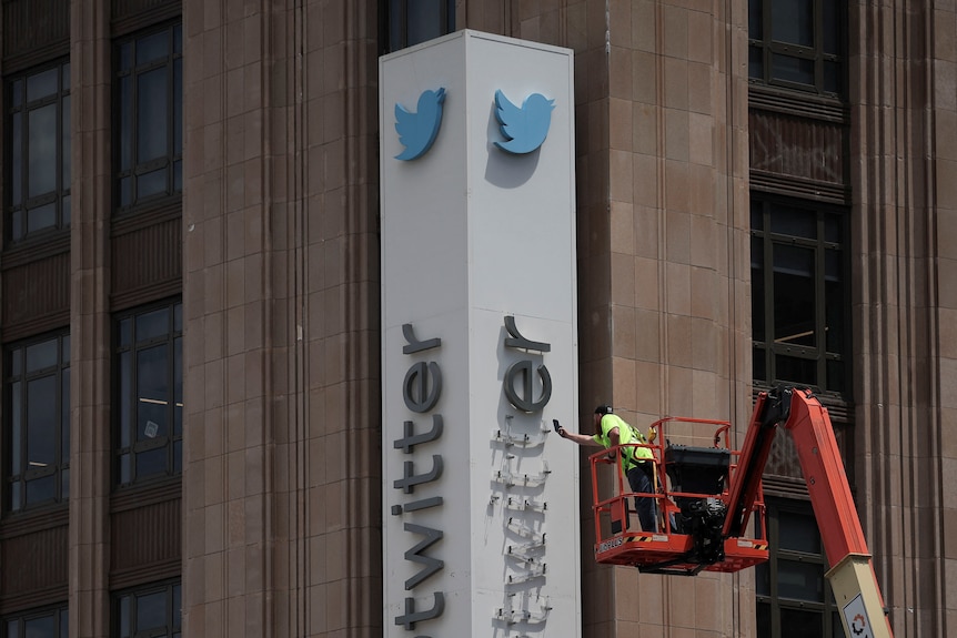 A worker stands in a cherry picker to removes each letter of the Twitter logo on the side of a building