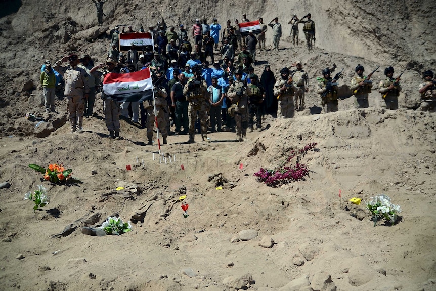 Iraqi soldiers stand next to a mass grave in Tikrit