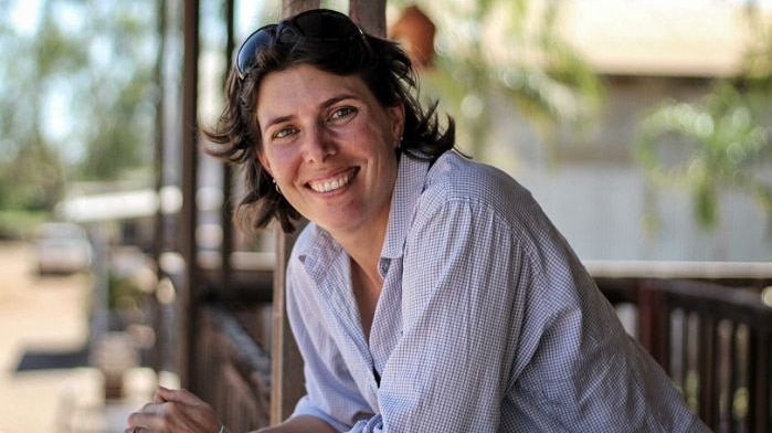 A woman smiles at the camera as she leans over a railing on a rural property