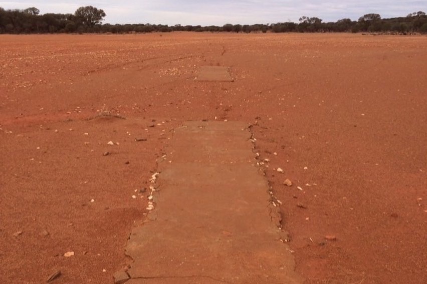 A cricket pitch covered in red dust and entirely surrounded by red dirt