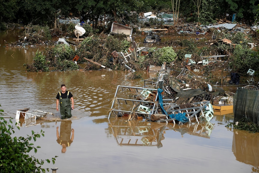 A man walks through floodwater surrounded by debris. 