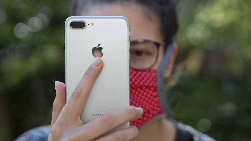 Young woman with protective mask looks at a mobile phone.