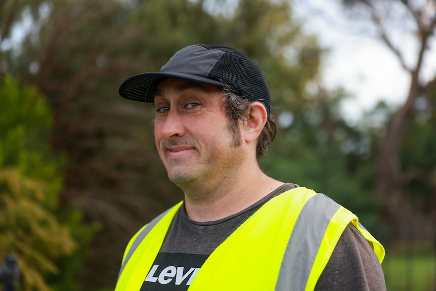 Ross Noble in a high vis vest wearing a cap. 