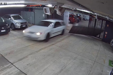 A white sedan knocks down the carpark gates as it speeds away from a gunman running behind