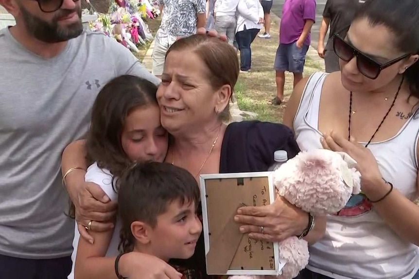 A woman holds two children in an embrace.