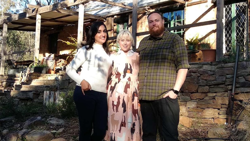 A young couple in interesting clothes with Del in front of a beautiful, bushy house