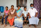 An Indian family sitting together on a bench looking solemn