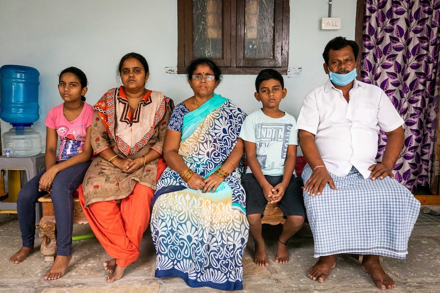 An Indian family sitting together on a bench looking solemn