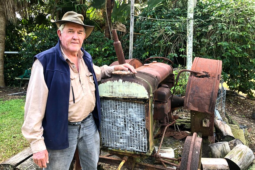 A man in a hat stands next to a rusty old tractor