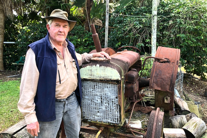 A man in a hat stands next to a rusty old tractor