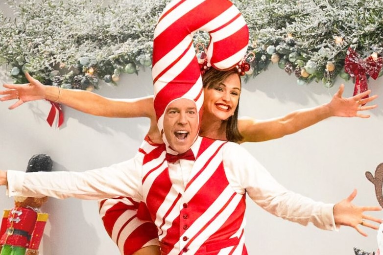 Jennifer Garner smiles, posing in a Christmas-themed photo with Ed Helms dressed as a candy cane.
