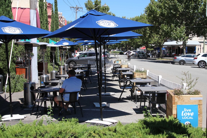 A solitary man sits at an outdoor cafe on a warm summer day.