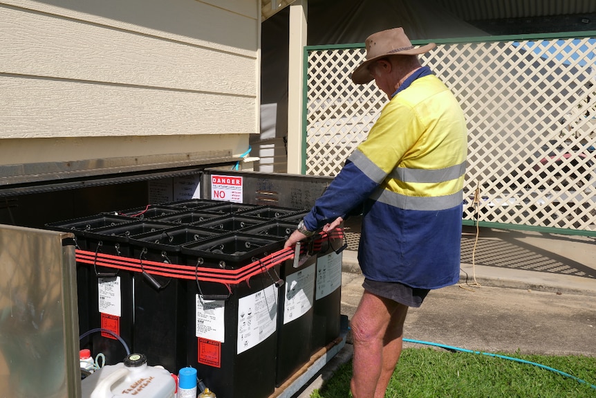 Trevor wearing a high vis shirt and hat, pulling on a group of big black boxes which are batteries.