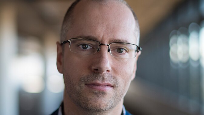 Man with glasses staring down the barrel of the camera.