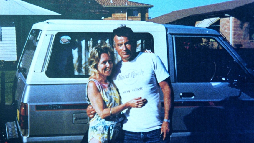 A woman and a man stand in front of a vehicle.
