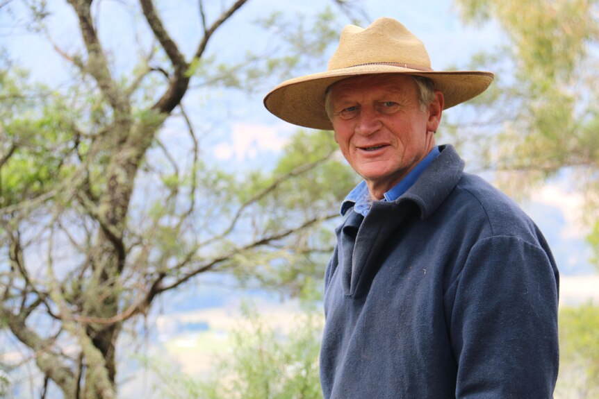 Martin wears a wide-brimmed hat and smiles among the trees.