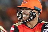 David Warner, wearing orange, plays a shot and looks over his right shoulder as Jos Buttler and Steve Smith stand behind in pink