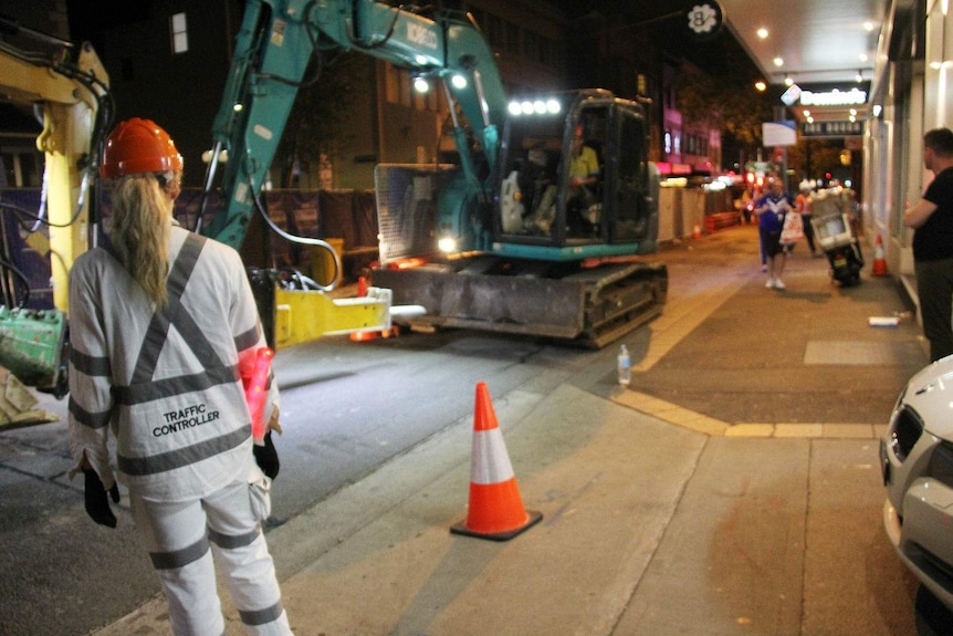 A female traffic controller in front of a construction site at night.
