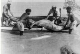 A black and white photo of four men hauling a crocodile into a boat in a river.