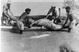A black and white photo of four men hauling a crocodile into a boat in a river.