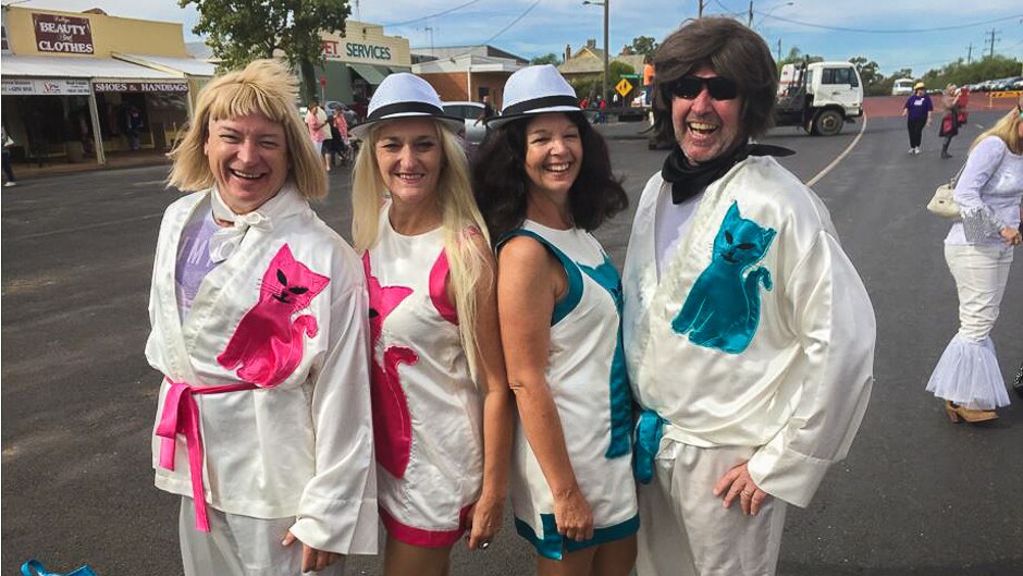 Two men and two women dressed in white ABBA costumes with satin cats on them