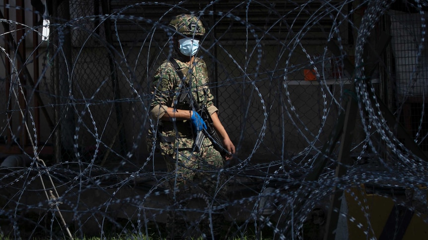 A soldier wearing a face mask is seen behind barbed wire in Kuala Lumpur.