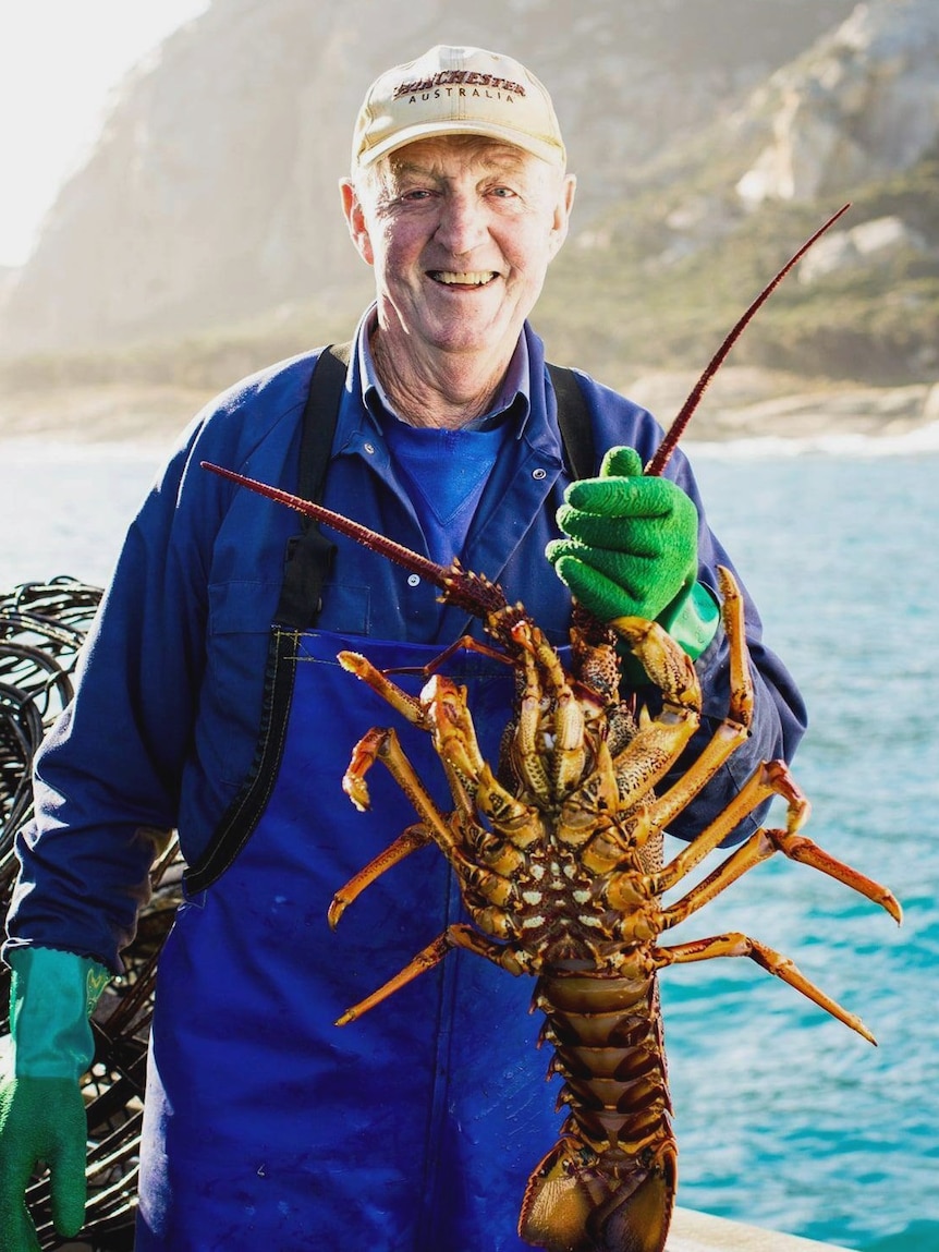 An elderly man holds a crayfish and smiles