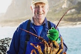 An elderly man holds a crayfish and smiles