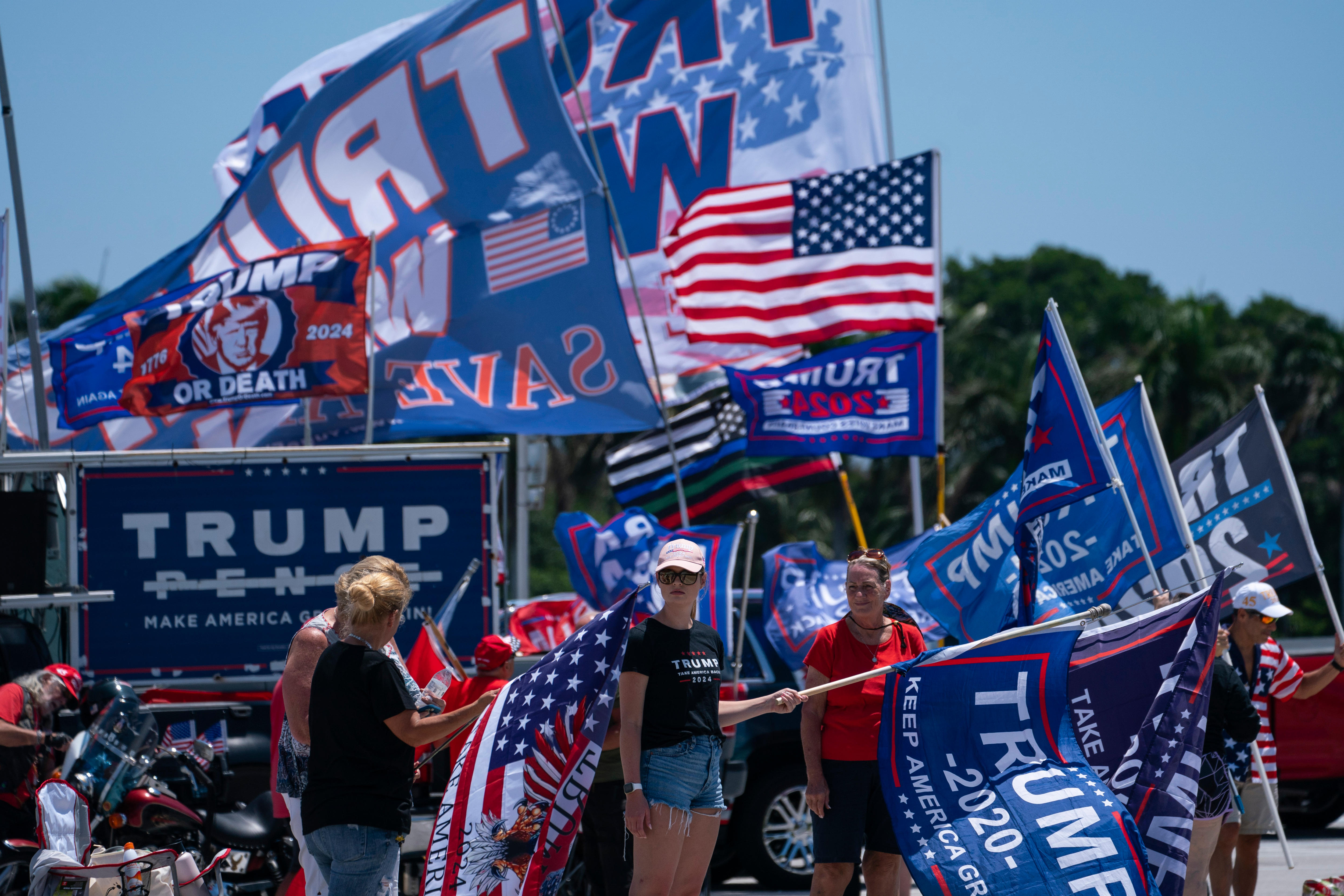 Trump supporters stand near US and Trump flags, mostly in red white and blue.