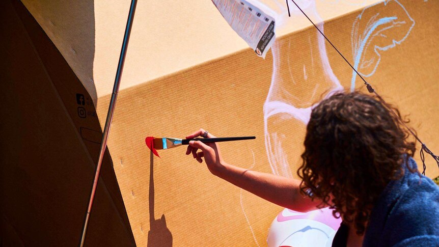 Woman painting a cardboard box which is a tent.