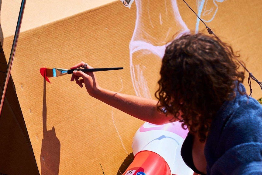 Woman painting a cardboard box which is a tent.