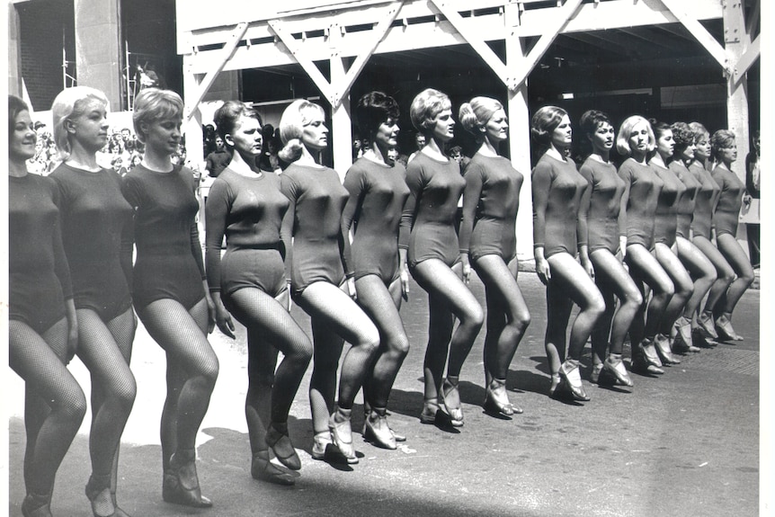 A black and white image of a line of women wearing long sleeved leotards and tights and dance shoes.