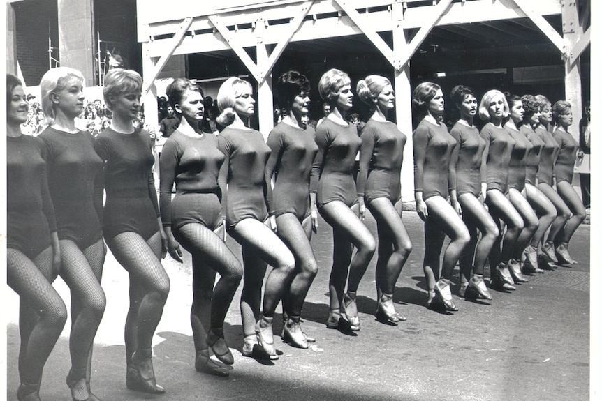 Une image en noir et blanc d'une ligne de femmes portant des justaucorps et des collants à manches longues et des chaussures de danse.