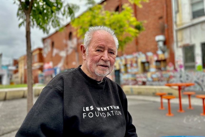 Man wearing a black sweater sitting at an outdoor table.