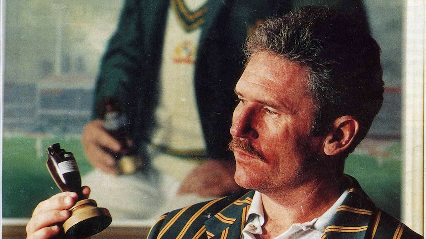 Alan Border pictured holding the ashes in front of his portrait painted by Paul Fitzgerald.