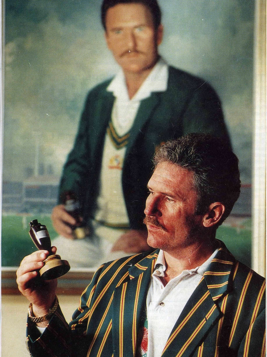 Alan Border pictured holding the ashes in front of his portrait painted by Paul Fitzgerald.