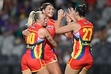 Three AFLW players come together and embrace, hug, clap hands, after scoring