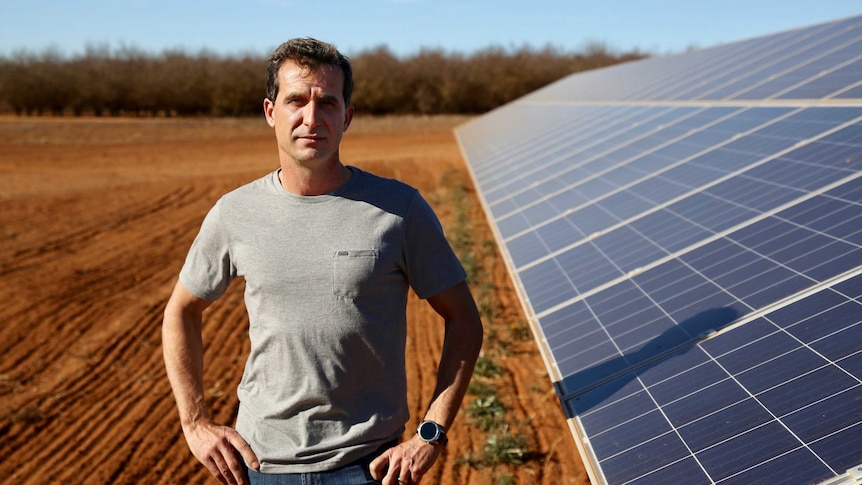 Drew Martin stands next to a solar panel.