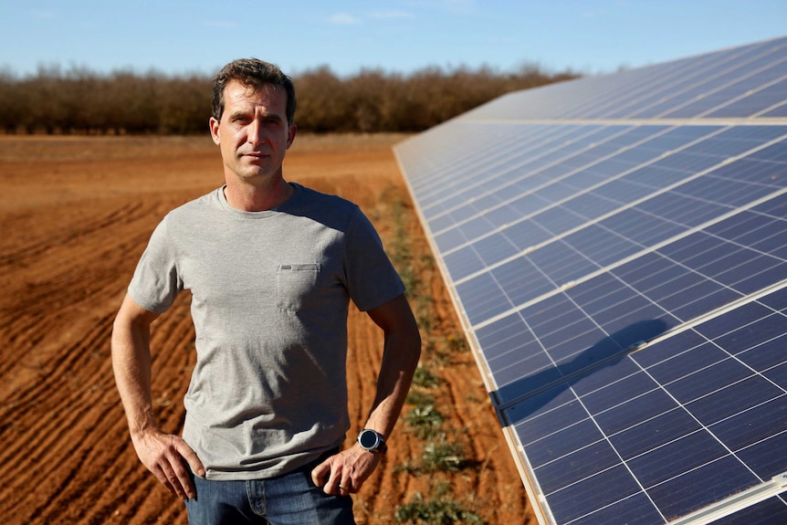 Drew Martin stands next to a solar panel.