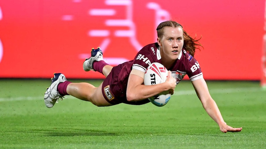 A Queensland player dives while holding the ball to score a try in the Women's State of Origin match against NSW.