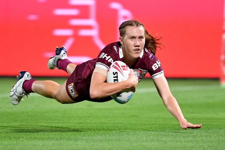 A Queensland player dives while holding the ball to score a try in the Women's State of Origin match against NSW.