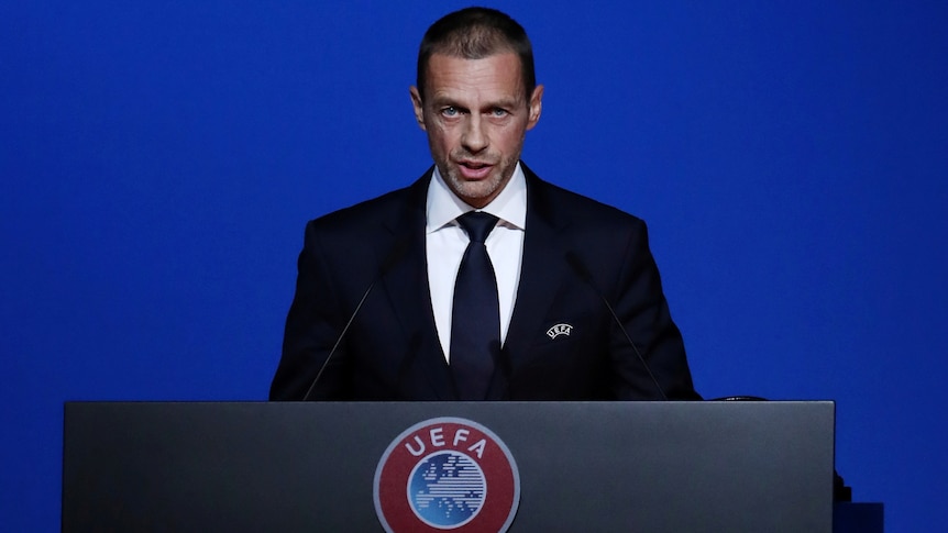 A man in a suit stands at a lectern with the UEFA logo on it.