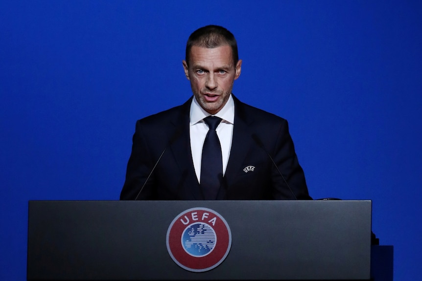 A man in a suit stands at a lectern with the UEFA logo on it.