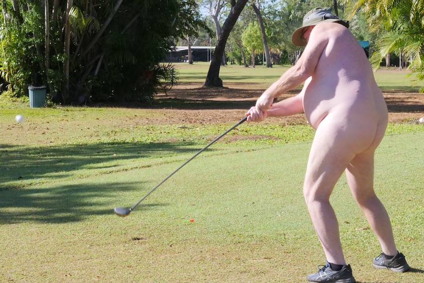 Elderly white man swings a golf club, wearing only a hat and shoes.