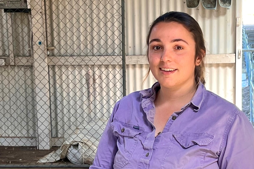 A young, dark-haired woman, smiling in a shearing shed.