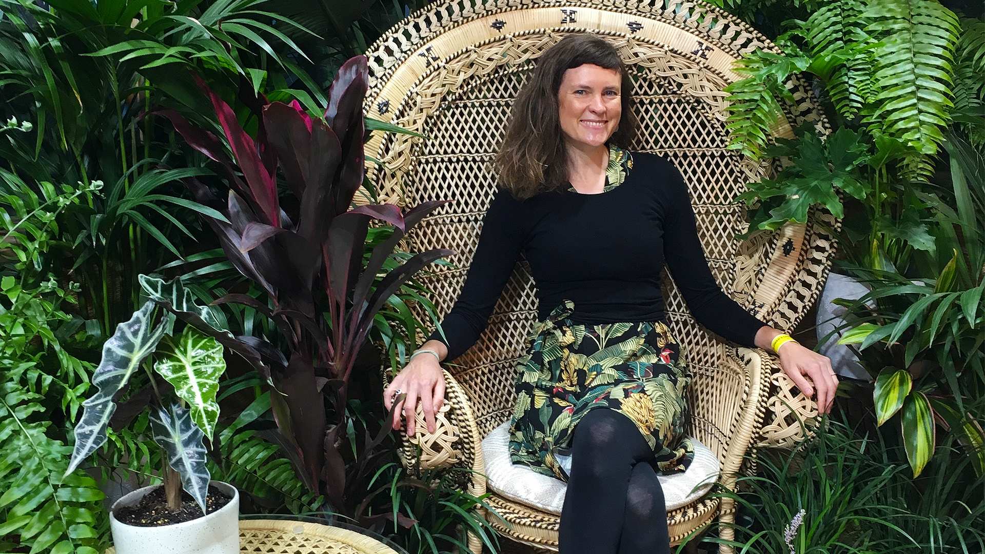 Lawyer-turned-indoor landscaper Alice Crowe sits on a rattan chair among a variety of lush plants.